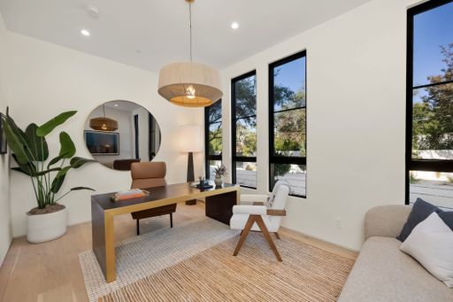 Modern home office with elegant decor, featuring a large desk, stylish chair, and natural light through tall windows.
