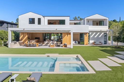 Modern luxury home with pool and spacious backyard, featuring sleek architecture and outdoor seating area under a clear blue sky.