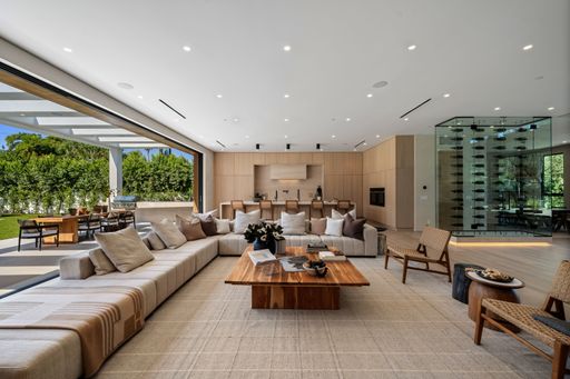 Luxurious modern living room with large sectional sofa, open to outdoor patio, featuring wine display and natural lighting.