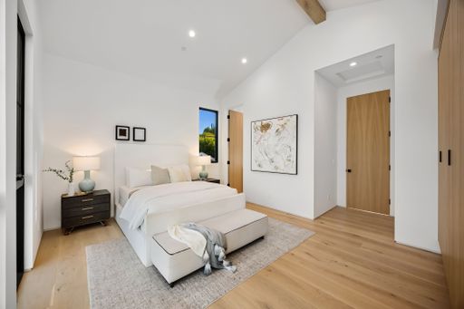 A modern, minimalist bedroom interior featuring a neatly made bed, wooden floors, and soft lighting, creating a cozy and inviting atmosphere.