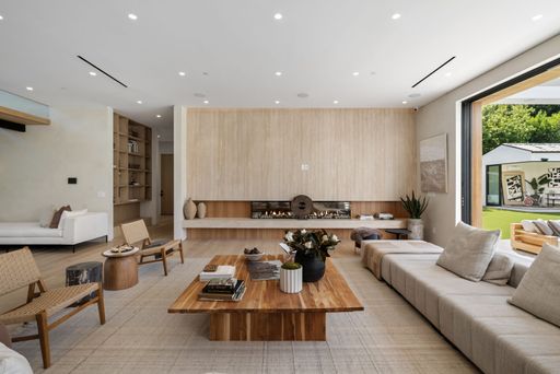 Modern living room with minimalist decor, featuring a wooden coffee table, neutral tones, and large windows opening to a garden.