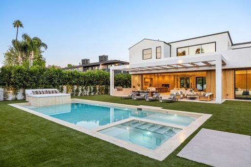 Modern luxury home with a spacious backyard, pool, and patio seating under a clear sky.