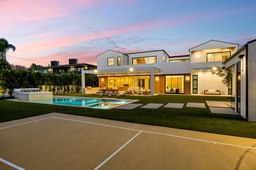 Modern luxury home exterior with pool and basketball court at sunset, showcasing elegant architecture and outdoor living space.