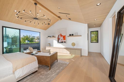 Modern bedroom with wooden ceiling, large window, and minimalist decor, featuring a stylish chandelier and natural light.