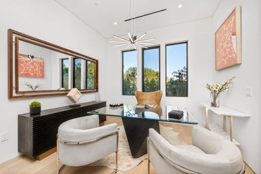Modern home office interior with elegant furniture, large windows, and stylish decor featuring a glass desk and contemporary artwork.