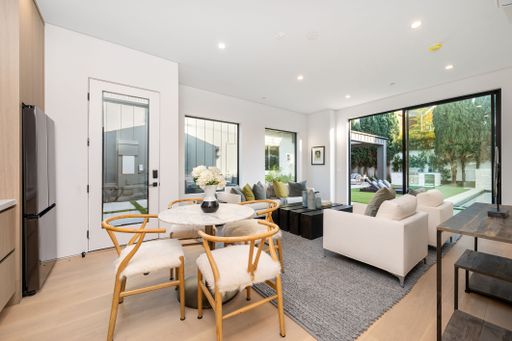 Modern living room with elegant decor, large windows, and a view of a lush garden, featuring a cozy seating area and dining table.