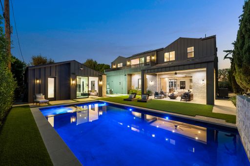 Modern luxury home exterior with illuminated pool at dusk, showcasing sleek architecture and outdoor living space.