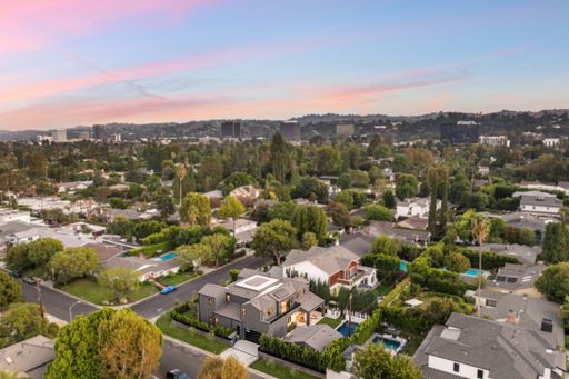 Aerial view of a suburban neighborhood with modern homes and lush greenery under a colorful sunset sky.