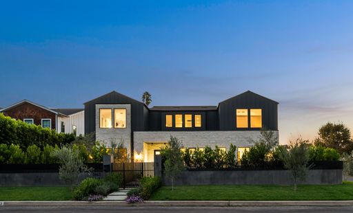 Modern luxury home exterior at dusk with illuminated windows and a manicured garden in a suburban neighborhood.