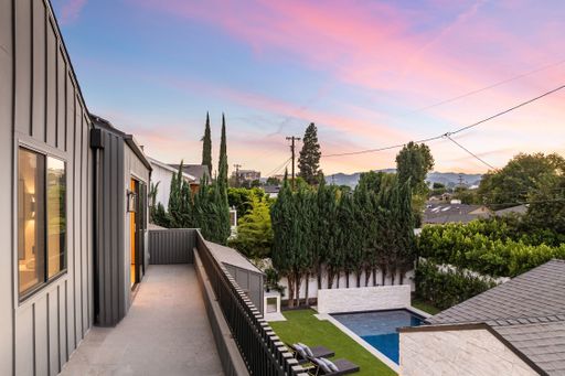 Modern home balcony view at sunset overlooking a landscaped backyard with pool and trees in a suburban neighborhood.