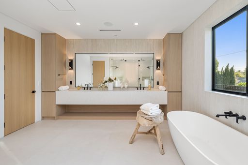 Luxurious modern bathroom interior with a freestanding tub, large mirror, and wooden accents, bathed in natural light.