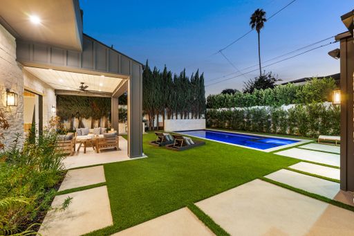 Modern backyard with a pool, patio seating, and lush greenery at dusk, showcasing outdoor living space and design.