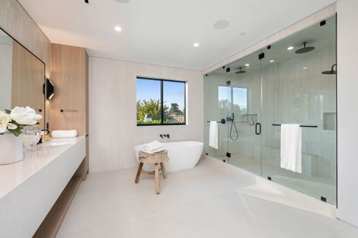 Modern luxury bathroom with a freestanding tub, glass shower, and natural light from a window, featuring minimalist decor.