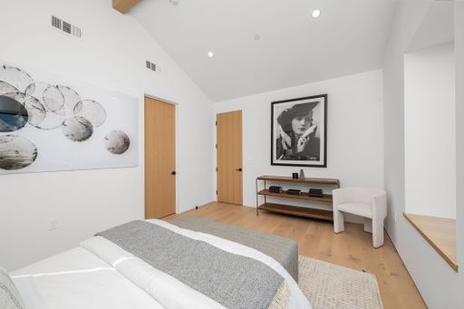 Modern bedroom interior with minimalist decor, featuring a large black and white portrait and abstract art on white walls.