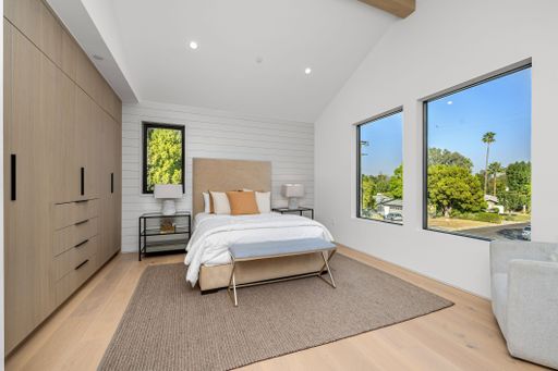 Modern bedroom interior with large windows, neutral tones, and natural light, featuring a cozy bed and stylish decor.