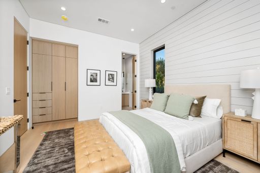 Modern bedroom interior with elegant decor, featuring a bed with green accents, wooden furniture, and natural light through a window.