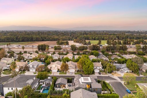 Aerial view of a suburban neighborhood with lush greenery and distant mountains under a colorful sunset sky.