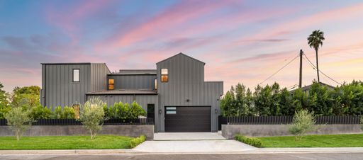 Modern gray house with lush greenery and a vibrant sunset sky in a suburban neighborhood.