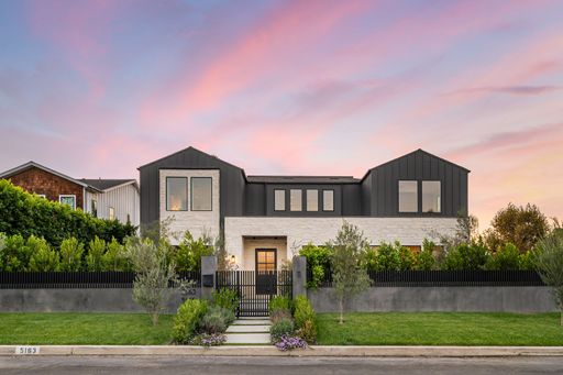 Modern suburban house with lush greenery and a vibrant sunset sky in a residential neighborhood.
