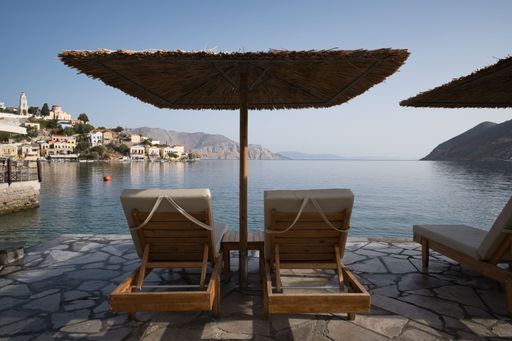 A tranquil seaside view with sun loungers and straw umbrellas overlooking a serene bay. Symi, Greece