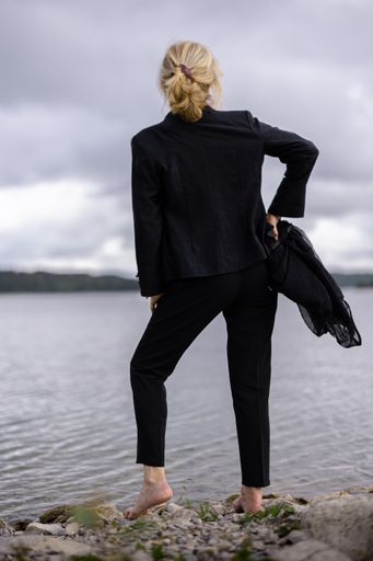A vertical shot of a blonde businesswoman from behind admiring the view of the sea on a gloomy day