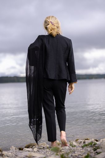 A back view of a cool barefoot woman in a black suit standing near a sea