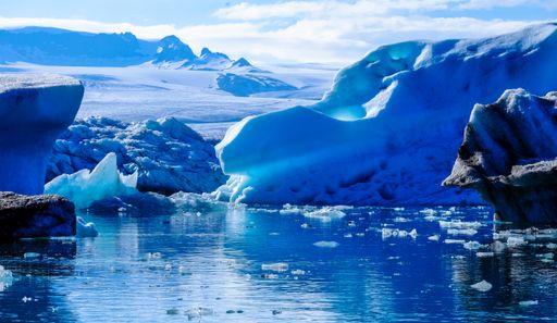 A beautiful shot of an ice burg near the water with cloudy sky in the background