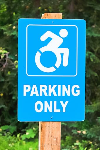 A closeup shot of a blue handicap parking only sign on a post with green trees in the background
