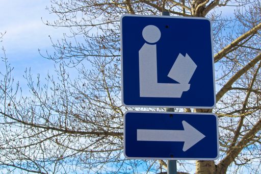A direction to library sign with tree in background