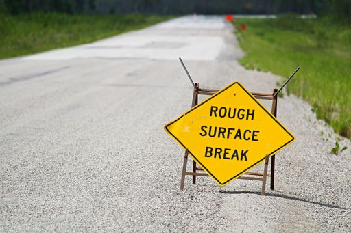 A yellow rough surface break sign with a road blurring into the background