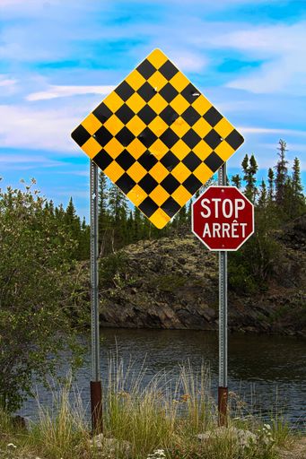 A vertical shot of checkered "no entry" and "stop" signs in both english and french
