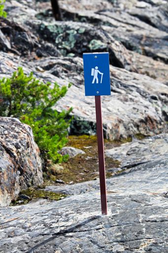 A vertical shot of a blue hiking trail sign over rough rocks