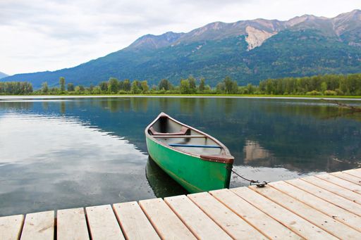 A canoe tied to the wooden dock on the lake surrounded by the mountains in Canada