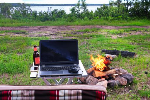 A cozy open-air atmosphere with a laptop and a drink near the bonfire on the coast of the lake