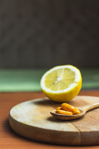 A spoon of pills next to a lemon on a wooden surface
