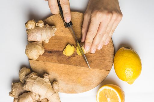 An overhead shot of a person cutting ginger roots next to lemons on a wooden board