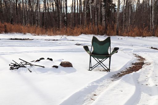 A camping chair in the snow beside a covered firepit