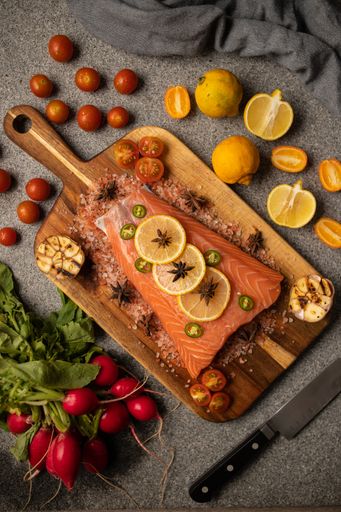 A vertical top view of a raw slice of fish with lemon slices and vegetables on it ready for cooking