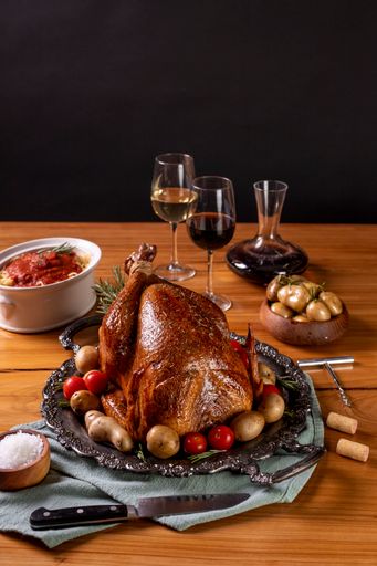 A vertical of a grilled chicken with potatoes served with glasses of wine on a wooden table