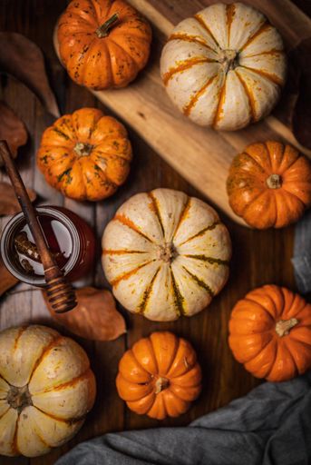 An overhead shot of many pumpkins with honey and dry autumn leaves on a wooden table