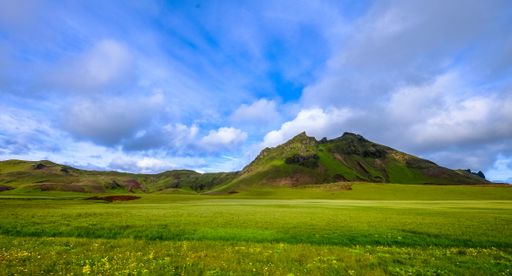 A grassy field with mountains in the distance under a cloudy sky