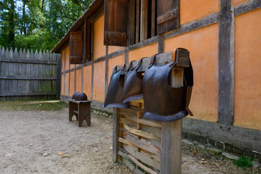 Medieval armor displayed outside a rustic wooden house with orange walls and a wooden fence in the background, evoking historical ambiance.