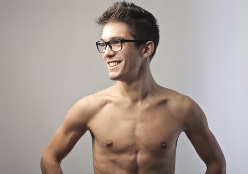 A closeup of a cheerful Caucasian man smiling in front of a gray background while shirtless