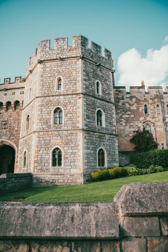 Historic castle tower with stone walls under a clear blue sky, surrounded by lush greenery.