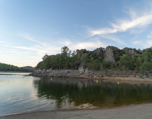 Reservoir surrounded by mountains and green vegetation with clouds reflecting on the water at sunset. Garcia Sola reservoir. Extremadura.
