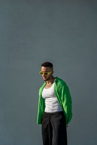 A vertical of a Spanish bearded attractive young male posing in stylish clothes on the gray background