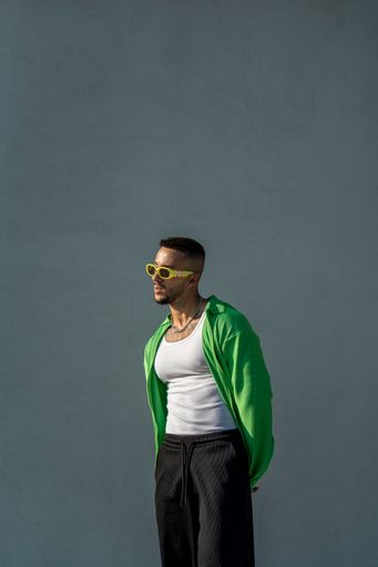 A vertical of a Spanish bearded attractive young male posing in stylish clothes on the gray background