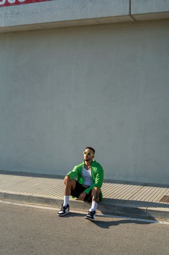 A Spanish bearded attractive young male sitting on the sidewalk posing in stylish clothes