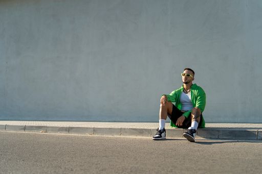 A Spanish bearded attractive young male sitting on the sidewalk posing in stylish clothes