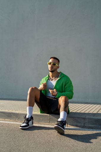 A Spanish bearded attractive young male sitting on the sidewalk posing in stylish clothes